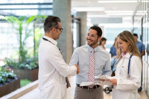 A hospital manager meets with two physicians in a hallway.