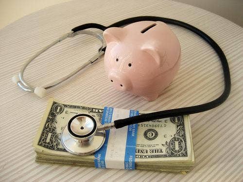 Piggy bank on table with stethoscope and stack of dollar bills.