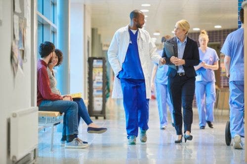 A healthcare consultant talks with a physician in a crowded hospital hallway.