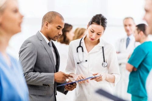 A hospital administrator meets with a physician in a crowded hallway.