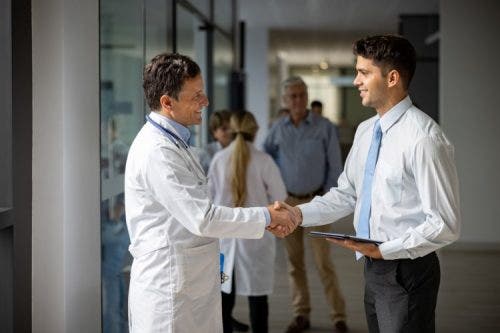 A healthcare policy analyst shakes hands with a physician in a hospital hallway.
