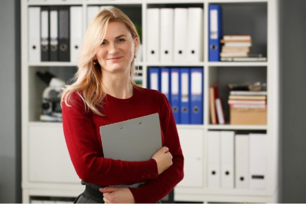 A former soldier and recent MBA graduate is standing in an office holding a clipboard.