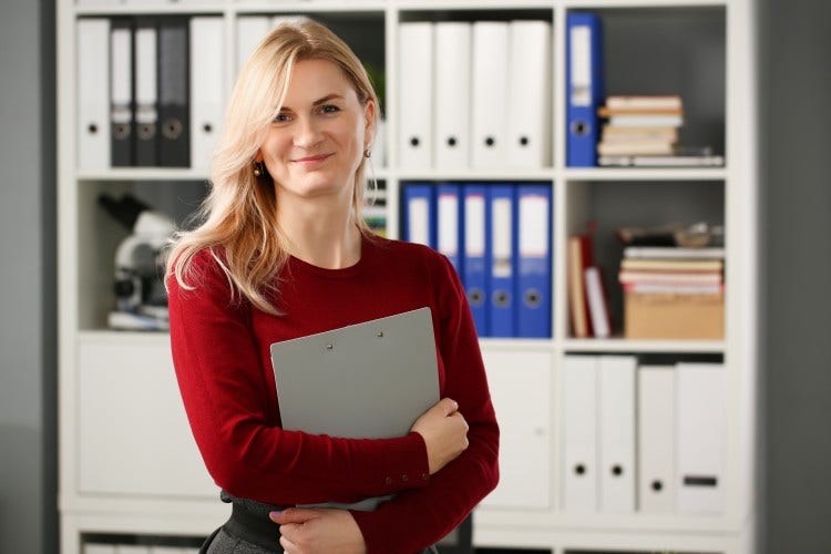 A former soldier and recent MBA graduate is standing in an office holding a clipboard.